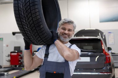 Garajda sakallı işçi tamir atölyesinde lastik tutuyor.