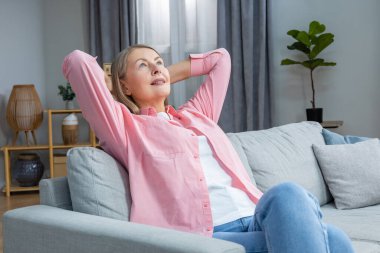 Memnun bir kadın. Pembe tişörtlü, orta yaşlı bir kadın evde vakit geçirirken mutlu görünüyor.