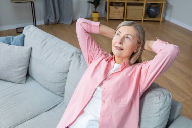 Memnun bir kadın. Pembe tişörtlü, orta yaşlı bir kadın evde vakit geçirirken mutlu görünüyor.