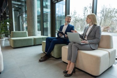 Yönetici ve meslektaşı koltukta dizüstü bilgisayar kullanarak ofis toplantılarında iş planlarını analiz ediyorlar.