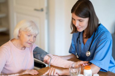 Tansiyonu ve nabzı olan yaşlı hastaya evde hipertansif tedavi için yardım sunan tıbbi uzman