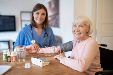 Hemşire evde bakım sağlayan tansiyon testi ve nabız ölçümü yaparak kıdemli hastaya yardım ediyor.