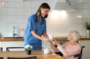 Ev ziyareti sırasında çay ikram ederek ve yardım ederek yaşlı hastaya yardım eden kadın hemşire