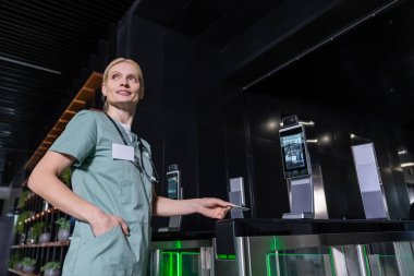 İşteki doktor. Sarışın genç doktor elinde giriş kartını tutuyor ve yan bakıyor.