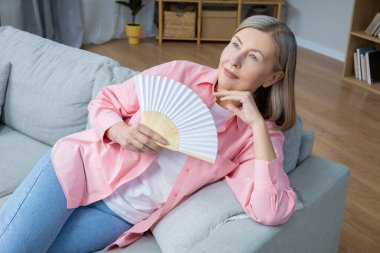 Hayranı olan bir kadın. Elinde vantilatörle koltukta oturan orta yaşlı bir kadın.