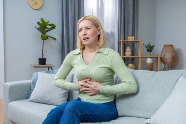 Mide ağrısı. Sarışın, orta yaşlı bir kadın kanepede oturuyor ve karın ağrısı çekiyor.