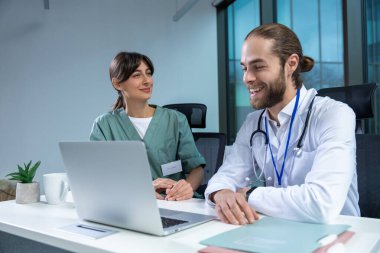 Hastane ofisindeki erkek ve kadın doktor teşhis ve bakımda teknolojiyi kullanarak iş birliği yapıyor.