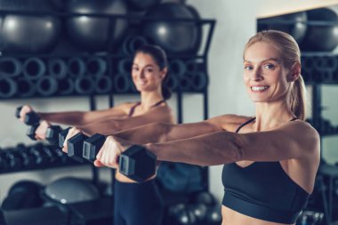 Strength workout. Women in sportswear standing with stretched arms holding dumb