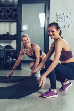 Antrenmandan önce. Spor kıyafetli iki beyaz kadın spor salonunda spor için paspas hazırlıyor.