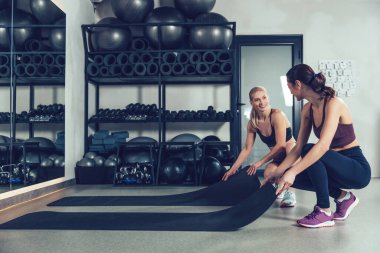 Antrenmandan önce. Spor kıyafetli iki beyaz kadın spor salonunda spor için paspas hazırlıyor.