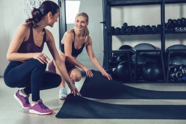 Antrenmandan önce. Spor kıyafetli iki beyaz kadın spor salonunda spor için paspas hazırlıyor.