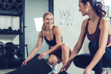 Antrenmandan önce. Spor kıyafetli iki beyaz kadın spor salonunda spor için paspas hazırlıyor.