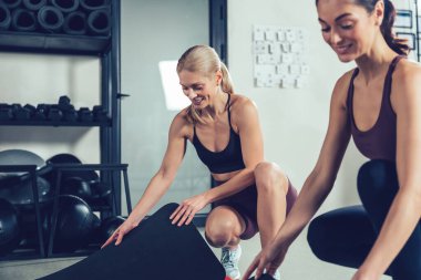 Antrenmandan önce. Spor kıyafetli iki beyaz kadın spor salonunda spor için paspas hazırlıyor.