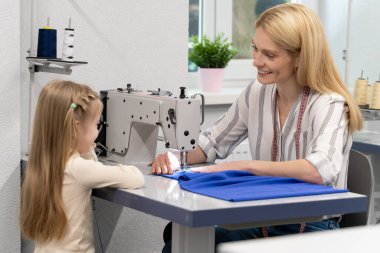 Anne ve çocuk. Sarışın, uzun saçlı, bayan elbise tasarımcısı, kızıyla birlikte stüdyoda.