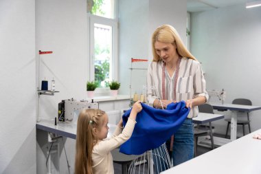 Anne ve çocuk. Sarışın, uzun saçlı, bayan elbise tasarımcısı, kızıyla birlikte stüdyoda.