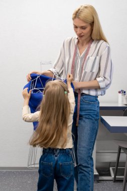 Anne ve çocuk. Sarışın, uzun saçlı, bayan elbise tasarımcısı, kızıyla birlikte stüdyoda.