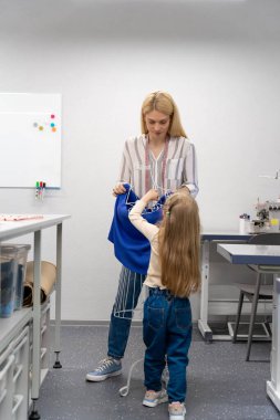 Anne ve çocuk. Sarışın, uzun saçlı, bayan elbise tasarımcısı, kızıyla birlikte stüdyoda.