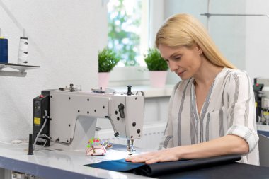 Dikiş dikiyorum Sarışın, sevimli bayan tasarımcı dikiş makinesinin başında oturuyor ve olaya dahil gibi görünüyor.