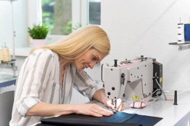 Dikiş dikiyorum Sarışın, sevimli bayan tasarımcı dikiş makinesinin başında oturuyor ve olaya dahil gibi görünüyor.