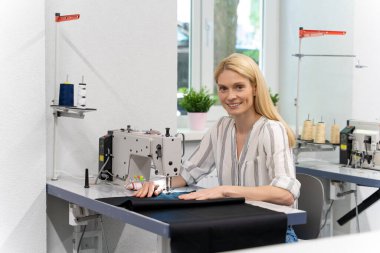 Dikiş dikiyorum Sarışın, sevimli bayan tasarımcı dikiş makinesinin başında oturuyor ve olaya dahil gibi görünüyor.