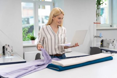 Tasarımcı. Sarışın, genç, beyaz elbise tasarımcısı kumaşla çalışıyor ve konsantre görünüyor.