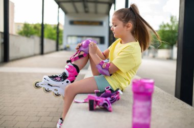 Küçük bayan patenci dışarıda kaymadan önce koruyucu giysiyi dizlerinin üstünde ayarlıyor.