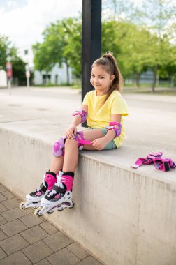 Küçük bayan patenci yaz aylarında dışarıda paten kaymak için koruyucu ekipmanla hazırlanıyor.
