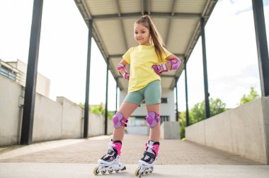 Küçük bayan patenci dışarıda paten sürerken eğleniyor paten becerilerini geliştiriyor.