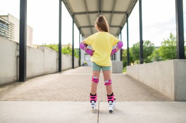 Küçük bayan patenci dışarıda paten sürerken eğleniyor paten becerilerini geliştiriyor.