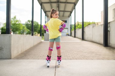 Stadyumun dışında buz pateni yapan küçük kız sağlıklı yaz aktivitelerinin tadını çıkarıyor.