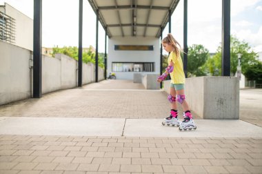 Küçük bayan patenci dışarıda paten sürerken eğleniyor paten becerilerini geliştiriyor.