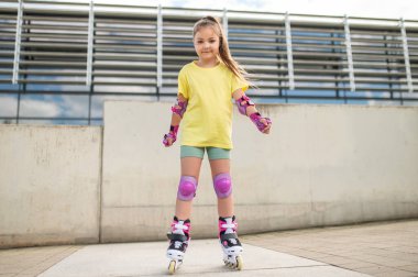 Stadyumun dışında buz pateni yapan küçük kız sağlıklı yaz aktivitelerinin tadını çıkarıyor.