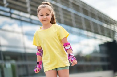 Küçük kız yaz boyunca stadyumun dışında paten kayarken eğleniyor.