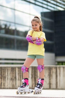 Küçük kız yaz boyunca stadyumun dışında paten kayarken eğleniyor.