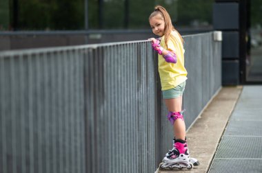 Küçük kız yaz boyunca stadyumun dışında paten kayarken eğleniyor.
