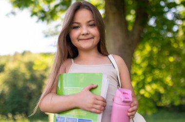 Güzel bir bayan çocuk, elinde kitaplarla dışarıda, huzurlu bir bahar parkında.