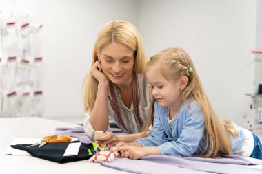 Küçük tasarımcı. Şirin sarışın çocuk tasarım stüdyosunda yeni bir modeli kesiyor.