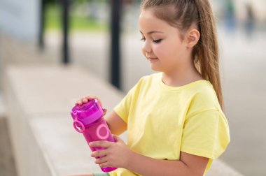 Küçük kız yaz tatilinin tadını çıkarırken şişeden su içiyor.