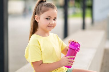 Şişeden su içen genç bir çocuk aktif yaşam tarzının keyfini çıkarıyor.