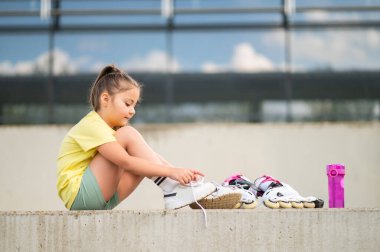 Paten giyen küçük kız dışarıda paten yapmaya hazırlanıyor. Yaz etkinliklerinin tadını çıkarıyor.