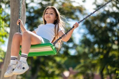 Yaz öğleden sonra parkta salıncakta neşeyle oynayan tatlı bir çocuk.
