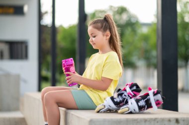 Patenli küçük bir kız, açık havada su içiyor ve yaz etkinliklerinin tadını çıkarıyor.