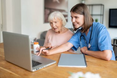 Huzurevindeki hemşire engelli yaşlı kadınla ilgileniyor. Birlikte dizüstü bilgisayar kullanıyorlar.