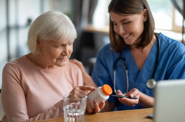 Genç dost canlısı hemşire klinikte ya da bakımevinde yaşlı kadın hasta ilaçlarını açıklıyor