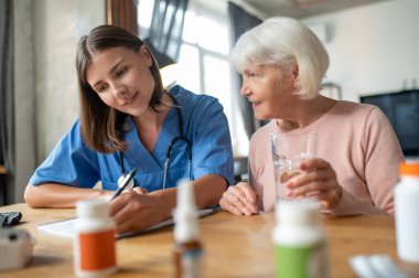 Kadın doktor, evde yaşlı bir hastayı ziyaret ediyor. Hastalık tedavisi görüyor ve tedavi görüyor.