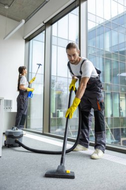 Elektrikli süpürge. Üniformalı genç adam konferans odasında yerleri temizliyor.