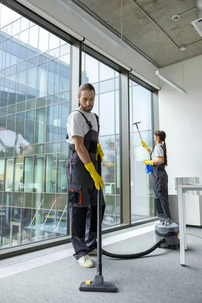 Elektrikli süpürge. Üniformalı genç adam konferans odasında yerleri temizliyor.