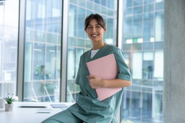 İşteki doktor. Elinde tıbbi geçmişi olan koyu renk saçlı, laboratuvar önlüklü bir kadın doktor.