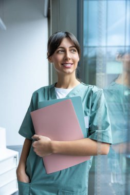 İşteki doktor. Elinde tıbbi geçmişi olan koyu renk saçlı, laboratuvar önlüklü bir kadın doktor.