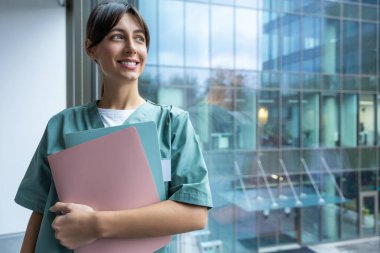 İşteki doktor. Elinde tıbbi geçmişi olan koyu renk saçlı, laboratuvar önlüklü bir kadın doktor.